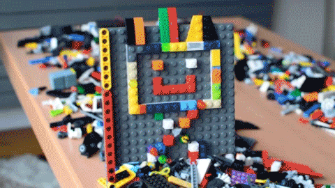 A GIF of two LEGO robots driving through bricks of LEGO, after which one robot falls off the table