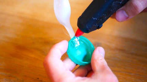 Image of a white plastic spoon being glued to a green milk bottle lid