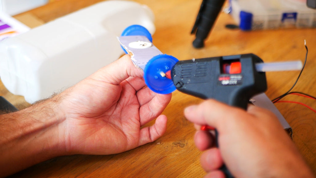 Image of a glue gun applying glue to a blue milk bottle lid