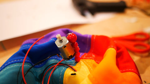 Photo of small electric motor attached to a line of beads sticking out of the top of a multicoloured hat 