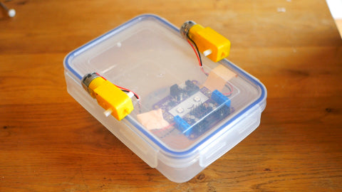 Image of a circuitboard attached to the inside of a Tupperware lid, along with two yellow motors attached to the lid of the container.