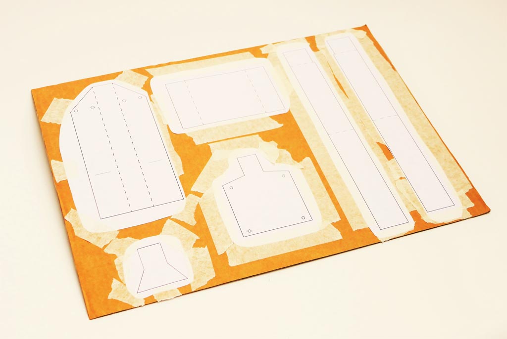 Image shows cardboard sheet with paper templates, that have been cut out , stuck down with tape on