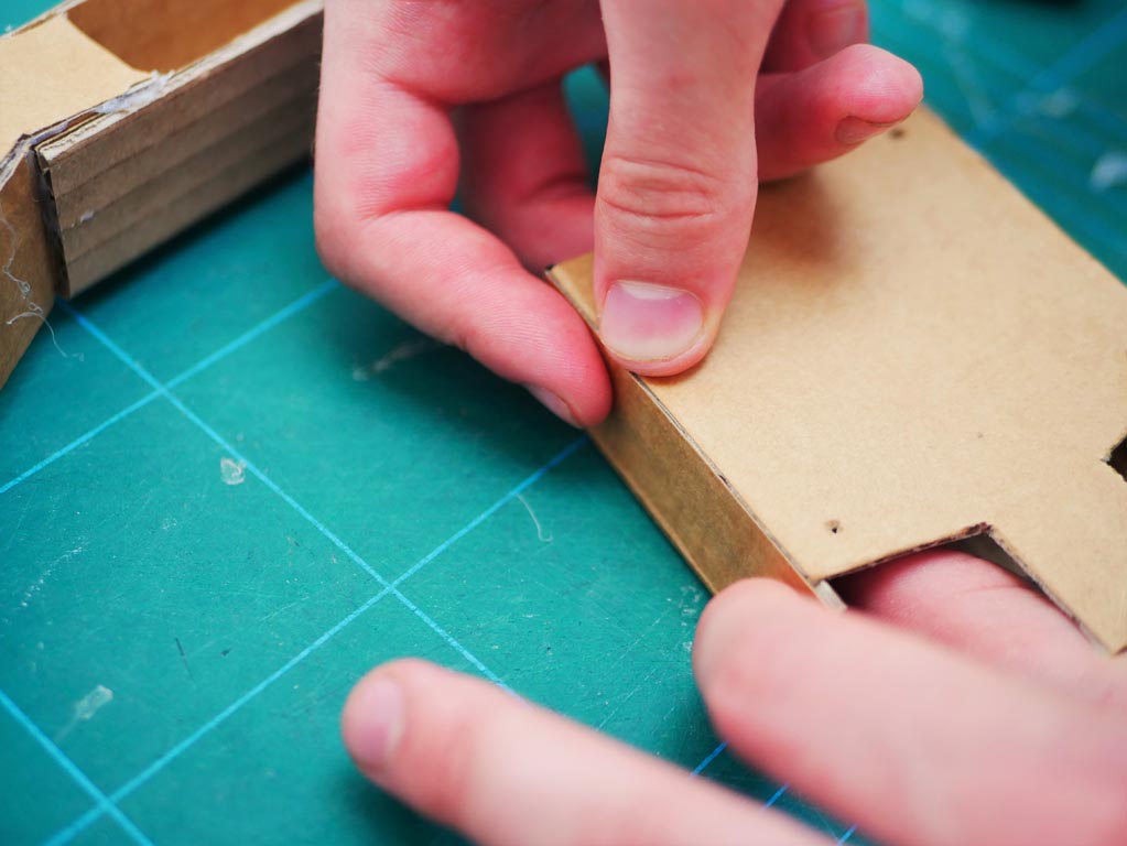 Image shows two pieces for box that holds batteries and bears circuit board being stuck together.