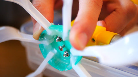 Image of a propeller that is made out of a green milk bottle lid and plastic spoons being screwed into a yellow motor.