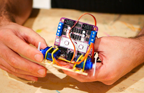 Image of a purple circuit board attached to a wooden structure and two blue servos.