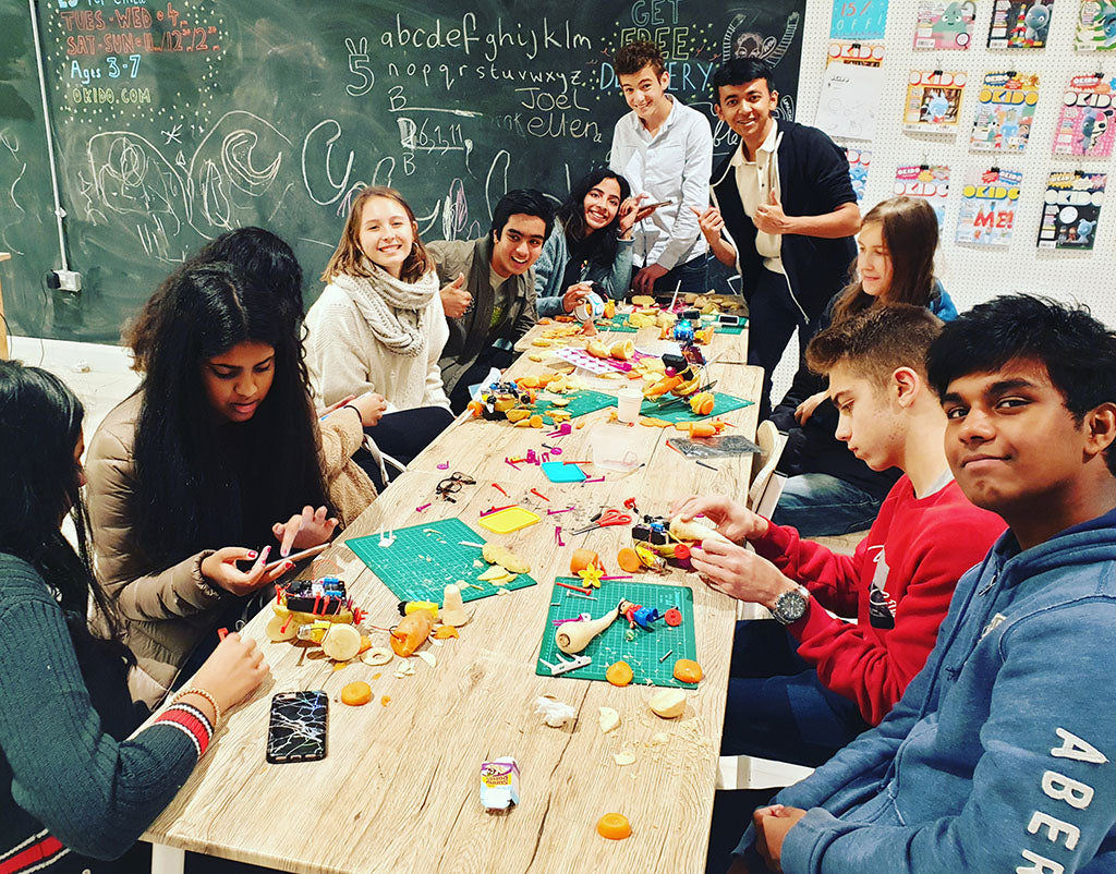 An image of a group of teenagers sitting on a table, making robots with several vegetables, including potatoes, carrots and parsnips.