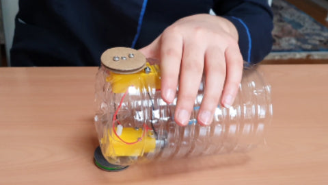 Image of half a plastic water bottle, with two yellow motors inside, and cardboard wheels attached to each motor