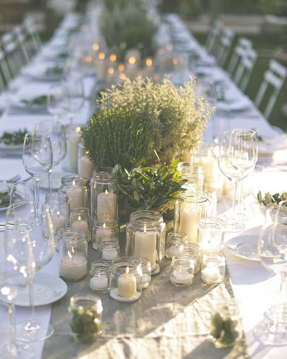 Close up of a table with white tablecloth, glasses and green foliage. 