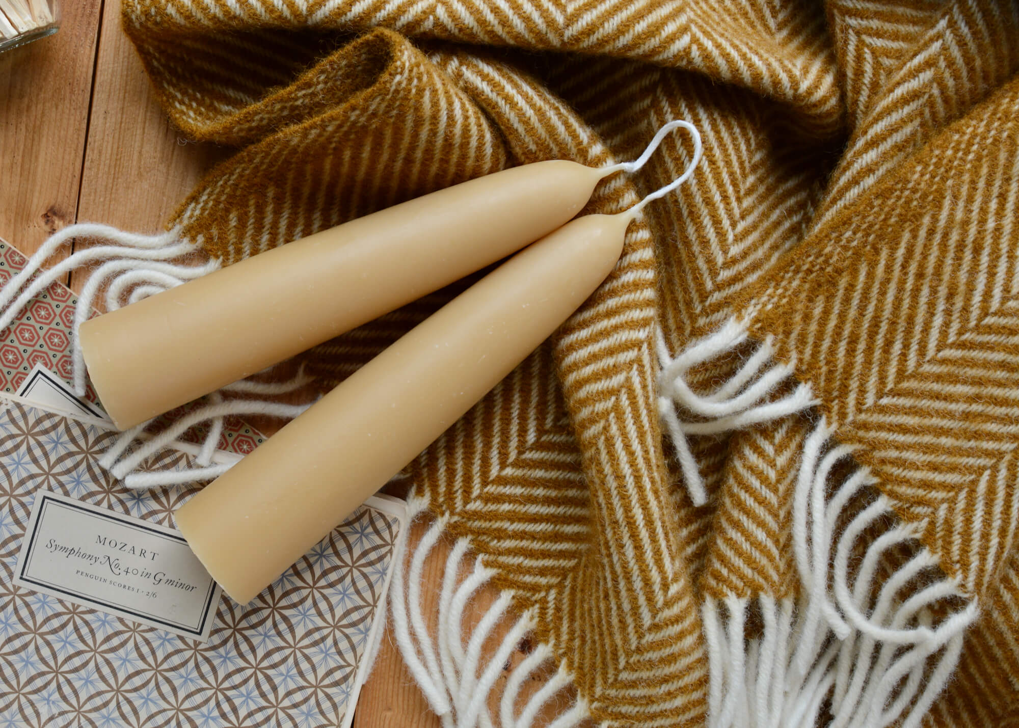 A pair of beeswax pillar candles, joined at the wick, on top of a ochre yellow wool blanket