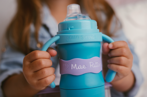 young girl holding Green Sprouts sippy cup with personalized name label