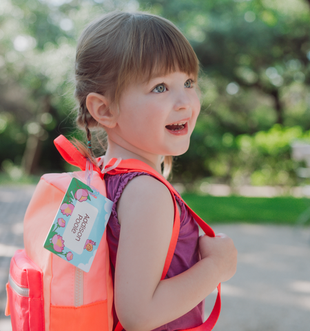 school aged child with personalized bag tag on backpack outside