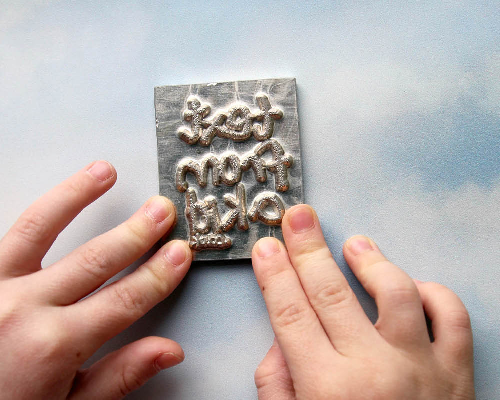 kids hands pushing a metal block die for foiling on a cloud background