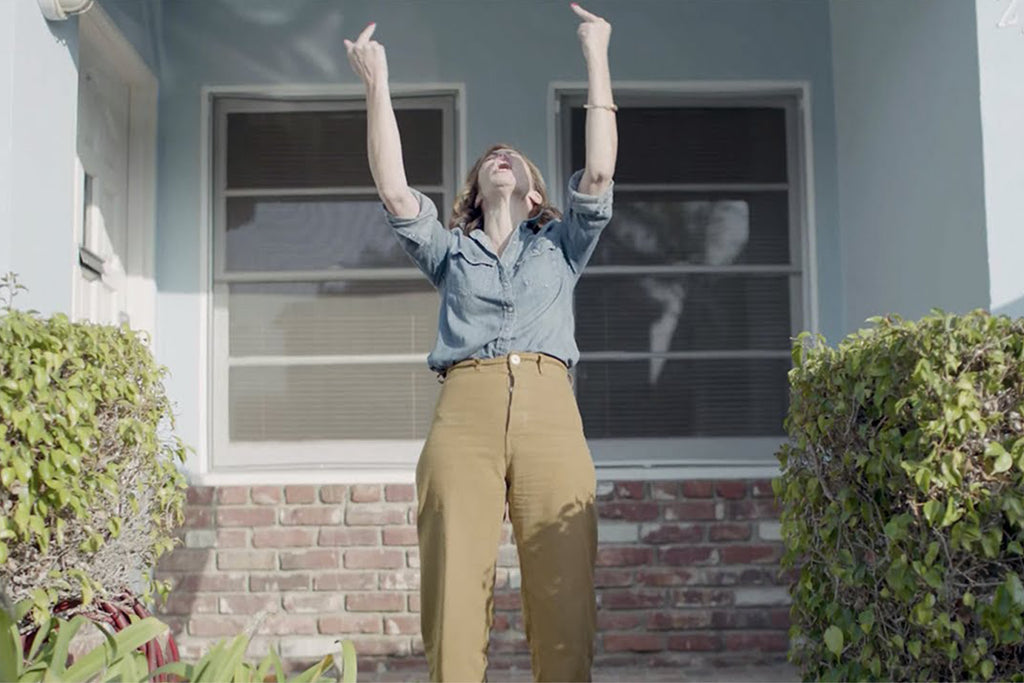 image of a female outside a house in a garden giving two middle fingers to teh sky