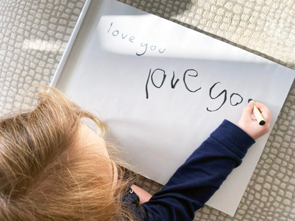 a kid writing love you on a large pad with oil pastels
