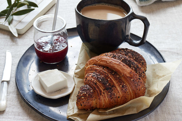A handmade croissant with fresh butter and jam on a bare salad plate along with a battuto mug filled with fresh morning coffee