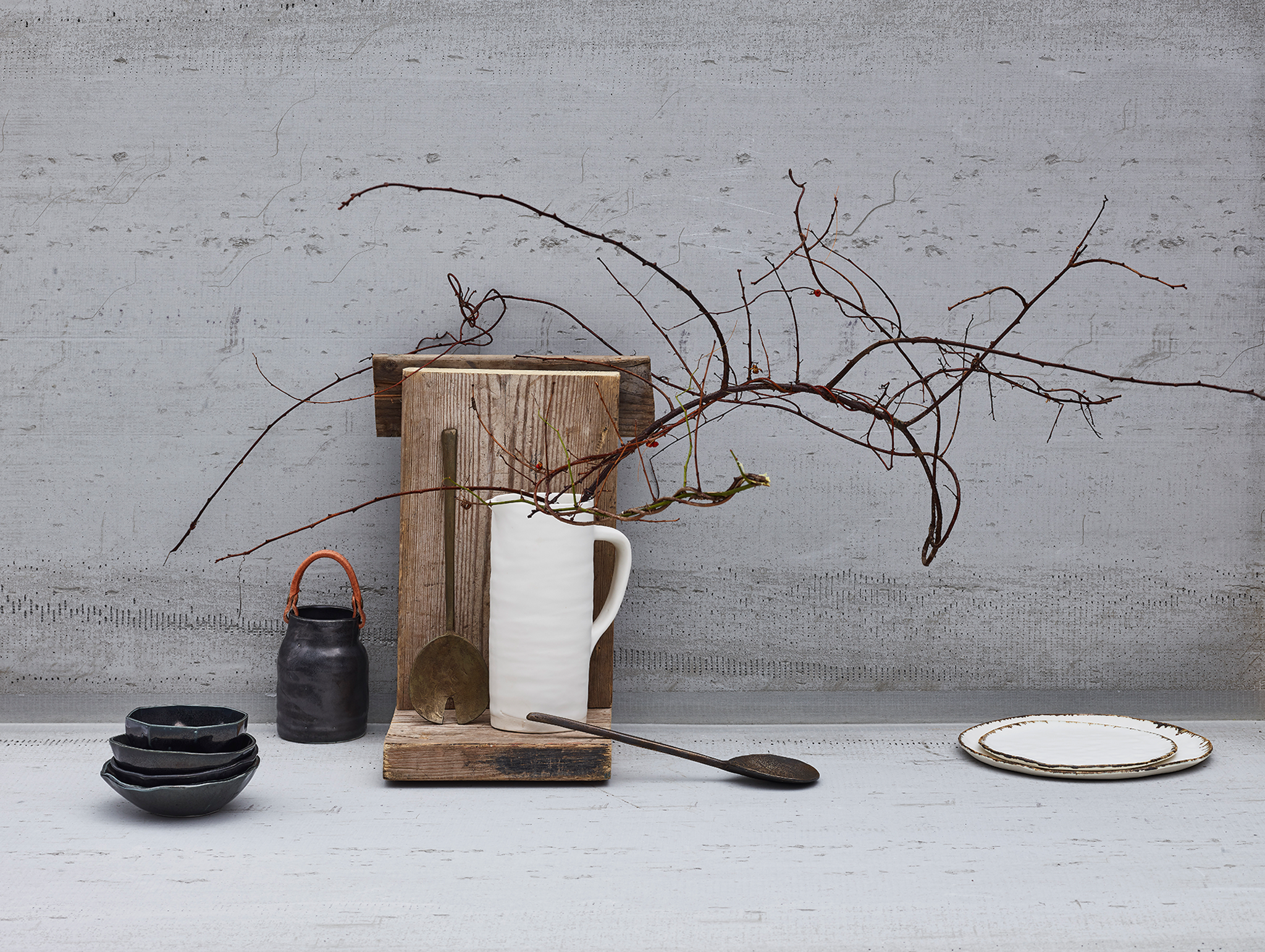 White ceramic pitcher with black ceramic bowls and bronze cast serving set on concrete background