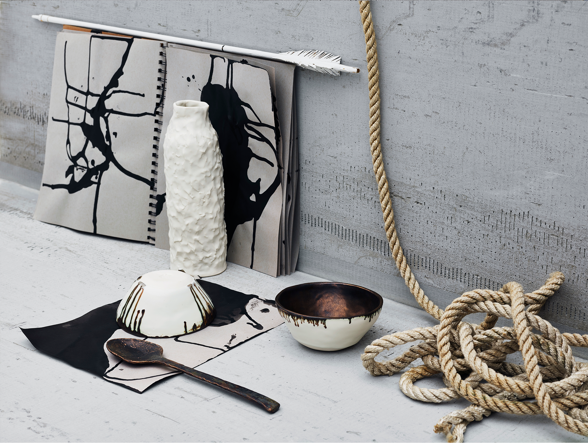 Textured white ceramic vase and bowls with bronze details on concrete background with rope, notebook, arrow and black ink