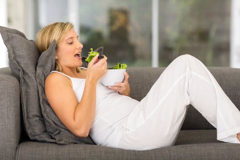 Pregnant woman laying on couch eating salad 