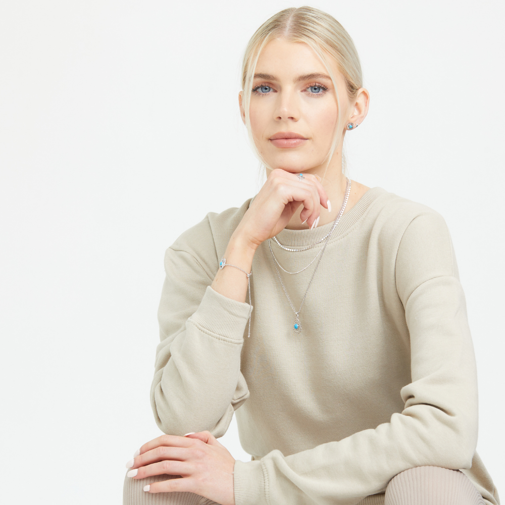 Woman wearing a light cream jumper and the FIYAH silver throat chakra jewellery collection