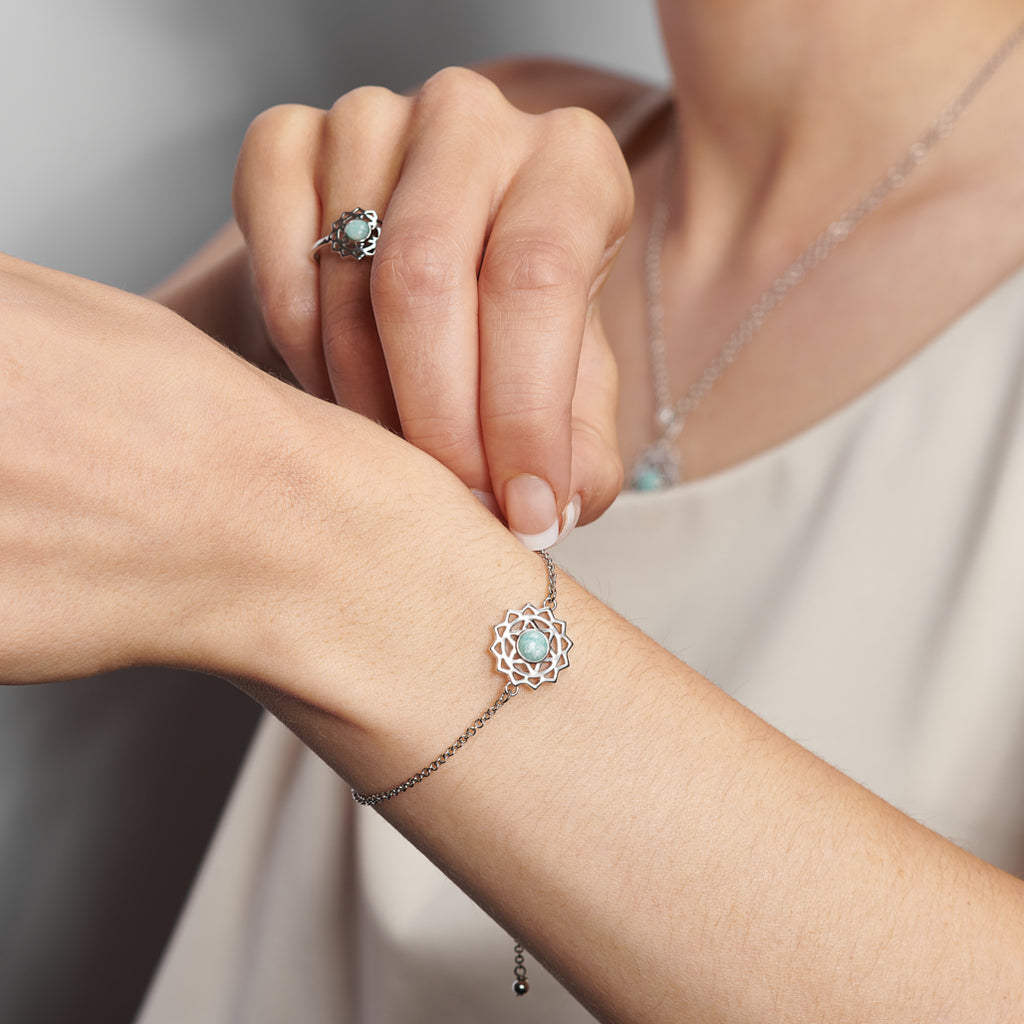 A close up of a woman's hand and wrist wearing the FIYAH heart chakra ring and bracelet