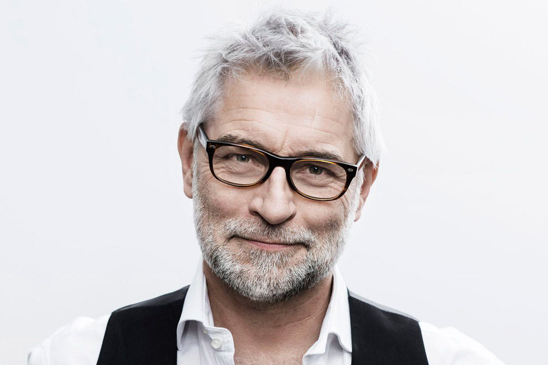 A grey haired man with grey beard wearing a rectangular dark tortoise eyeglasses frame