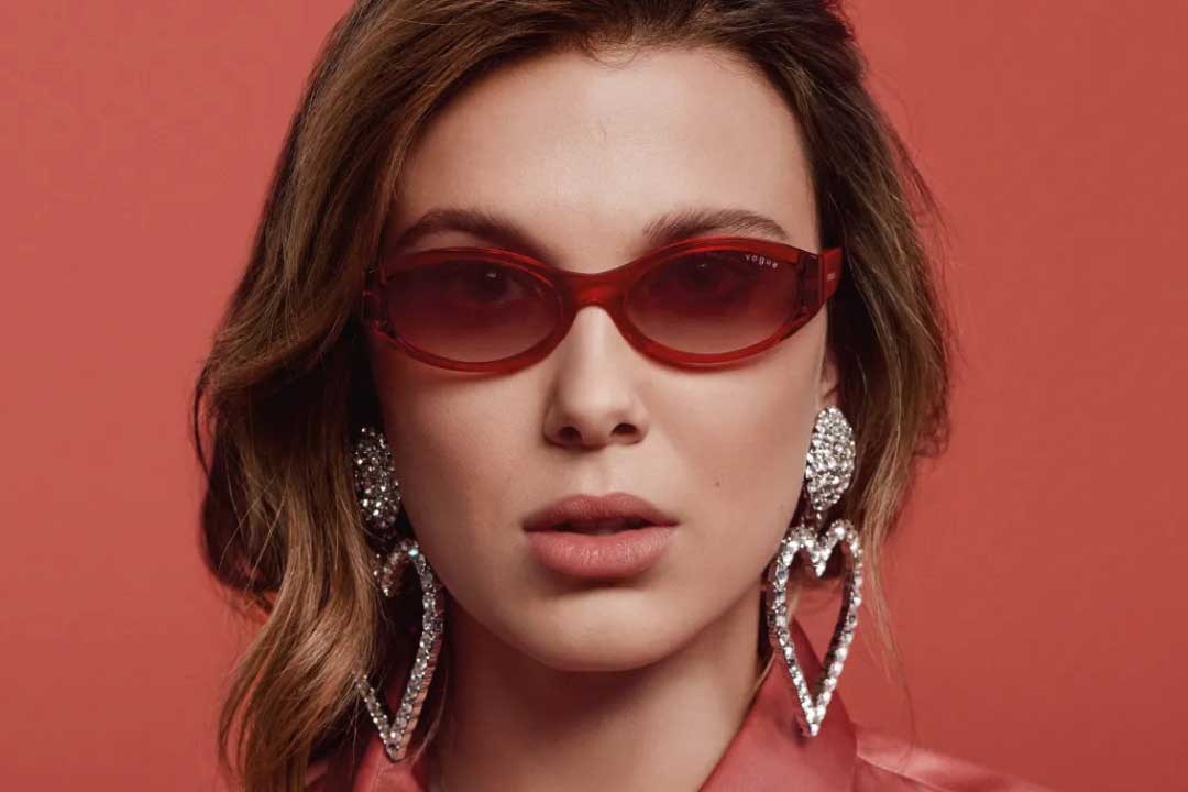 Actress Millie Bobby Brown wearing red sunglasses frame in front of red background