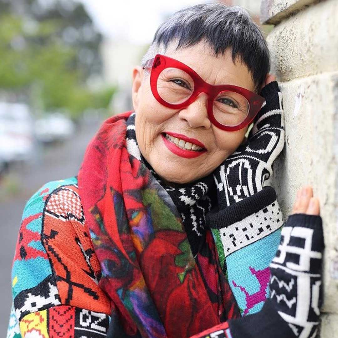 Asian lady with very short fringe haircut wearing multicolour jumper and bright red cat eye glasses frame