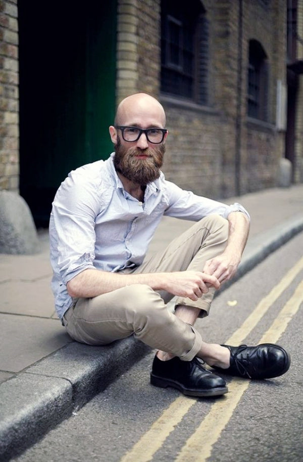 Bald man with glasses sitting on pavement in the street