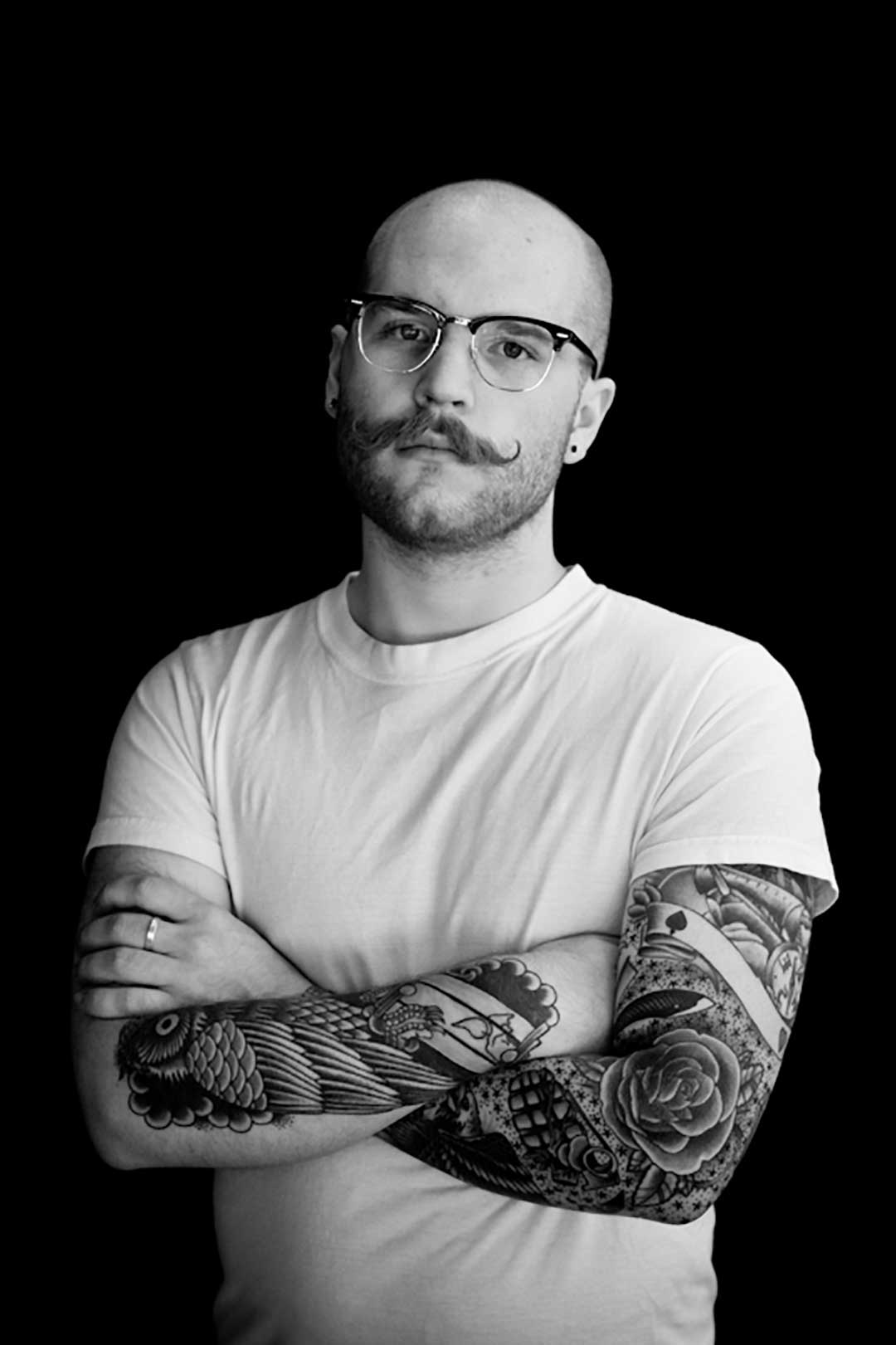 Bald man with moustache arms folded wearing white shirt and Clubmaster eyeglasses frame