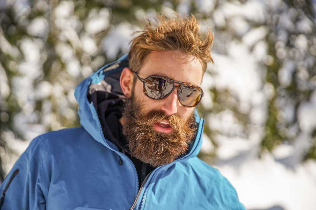 Bearded man in blue ski jacket wearing tortoise shell armless sunglasses frame
