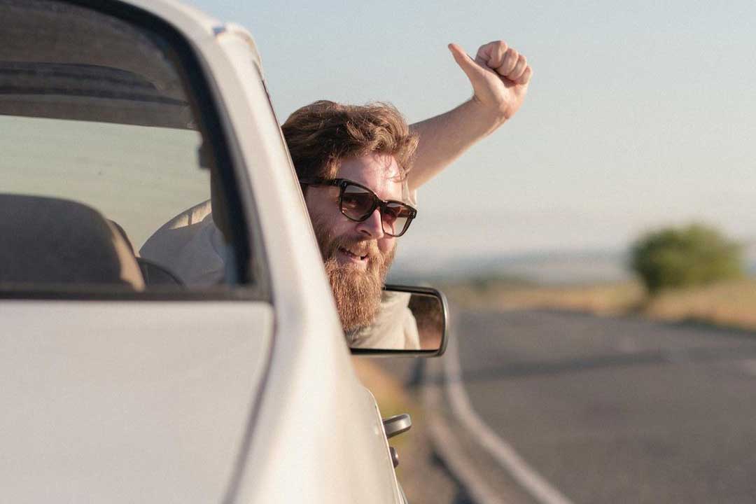 Bearded man leaning out of car window smiling wearing rectangular sunglasses frame