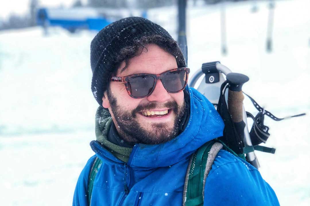 Bearded man wearing wool hat blue jacket and tortoise shell sunglasses frames on snowy day