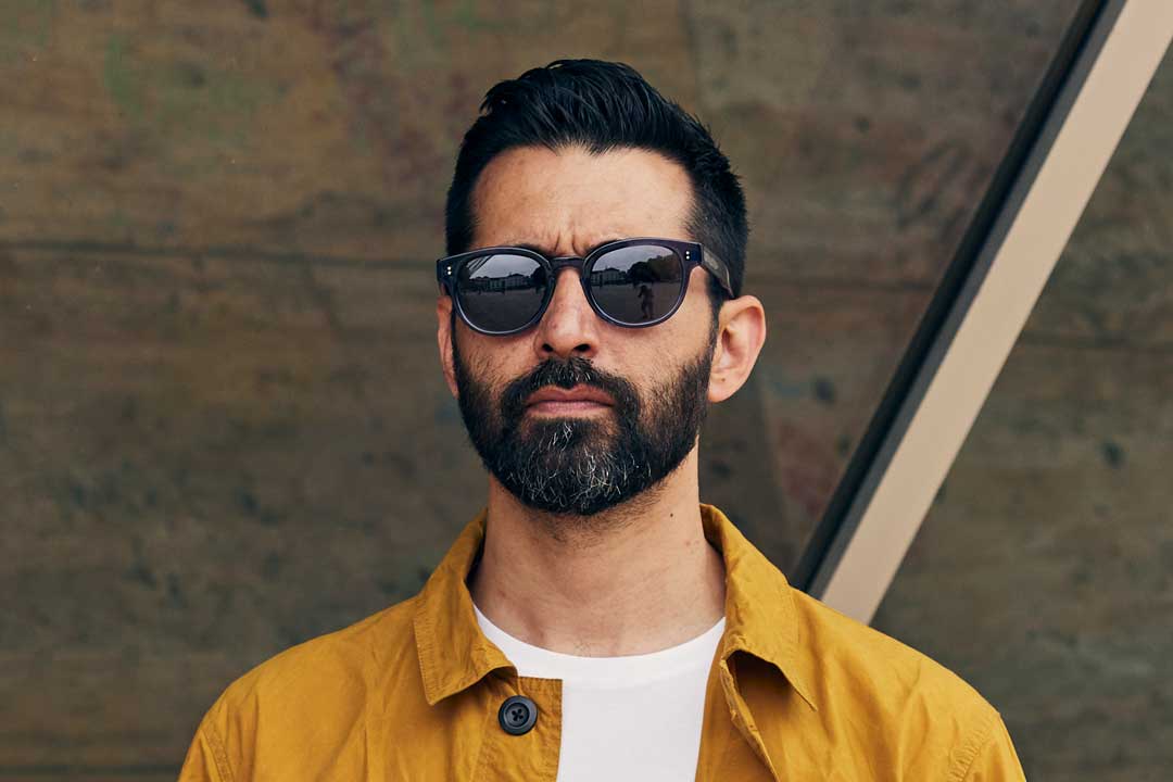 Bearded man wearing yellow jacket and oval blue sunglasses frame