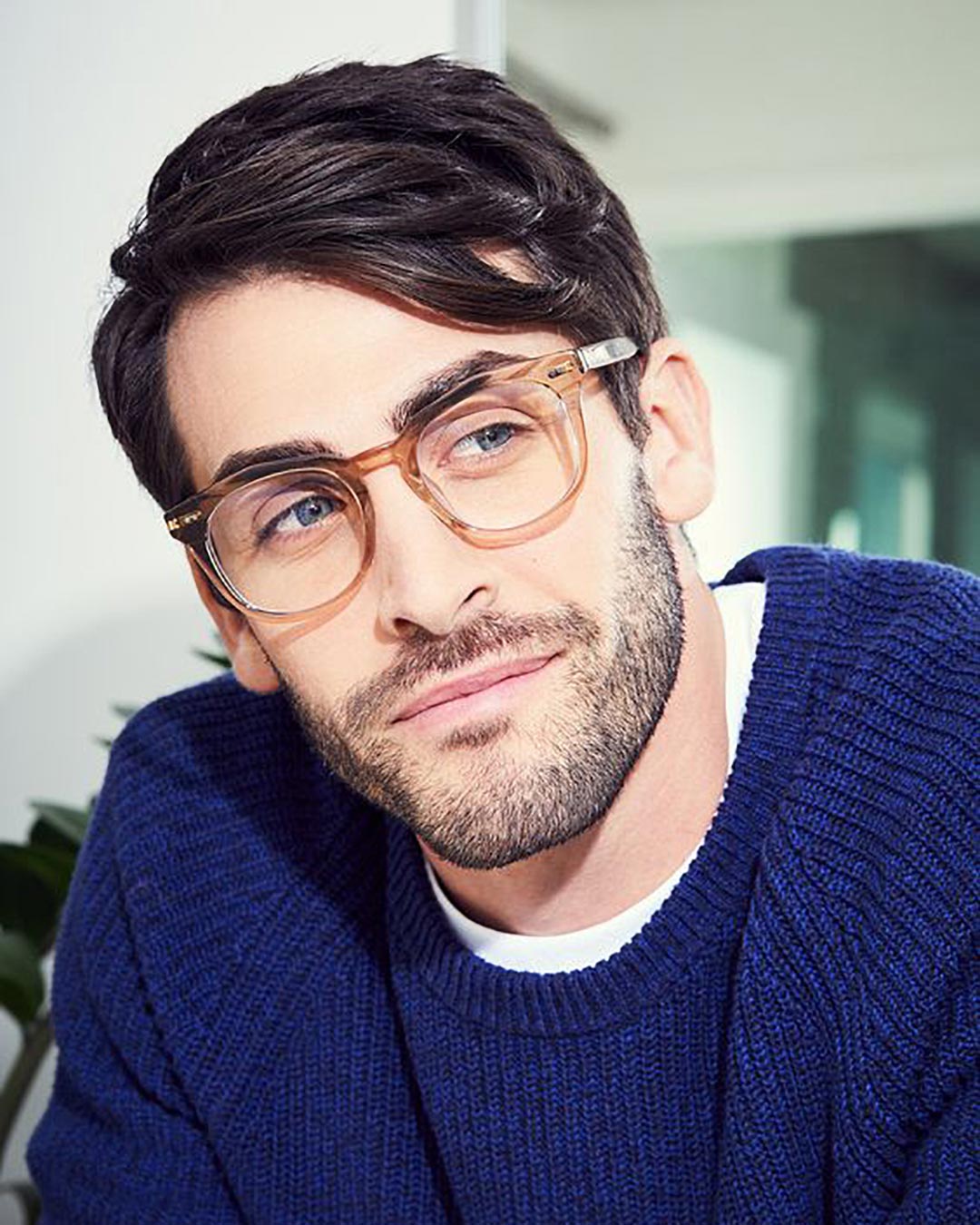 Bearded man with dark hair and blue jumper wearing chunky Wayfarer spectacles frame