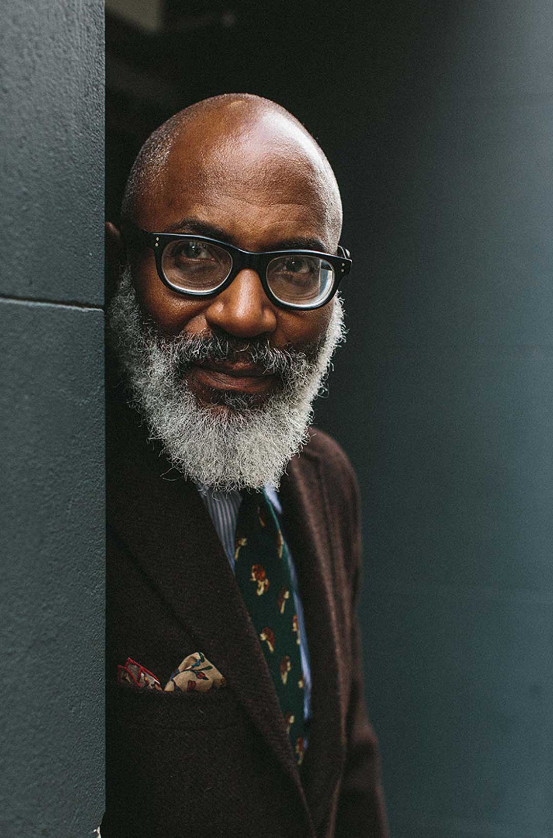 Bearded mature man standing in doorway wearing brown suit and thick black eyeglasses