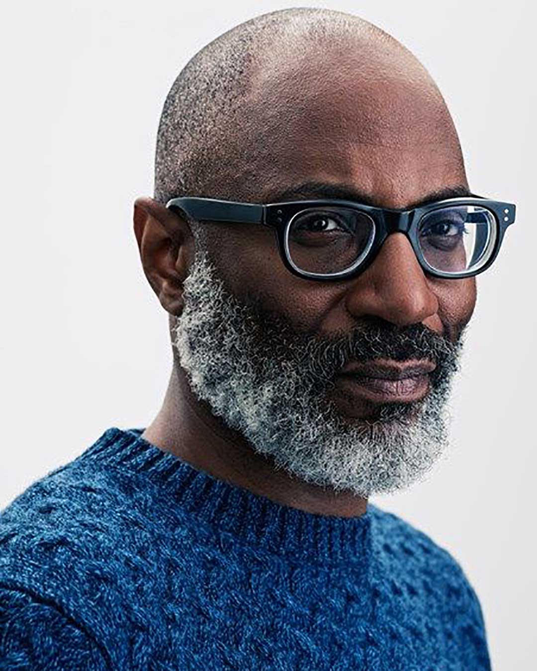 Black bald man in blue knitted sweater wearing thick black eyeglasses frame