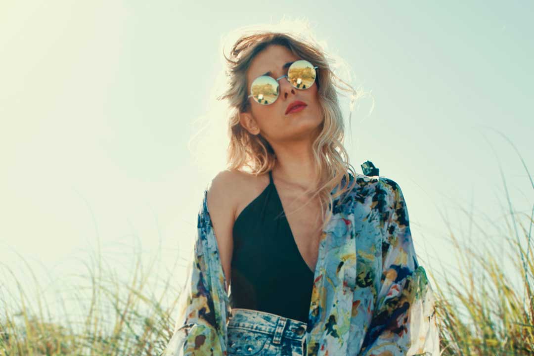 Blond lady at beach wearing floral serong and round mirror sunglasses on bright sunny day