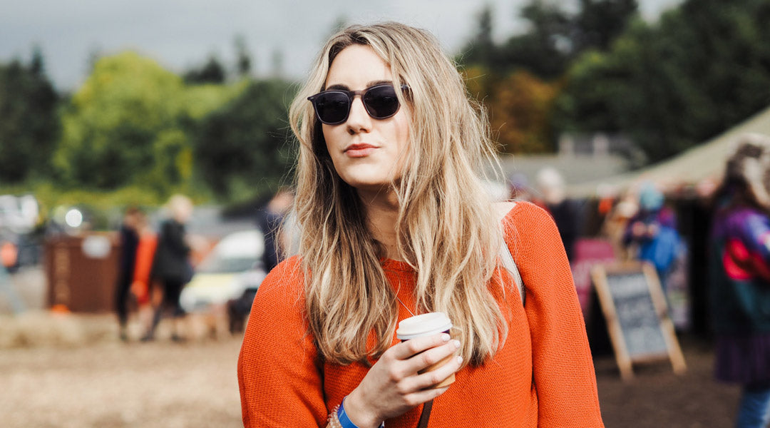 Blonde female at festival wearing orange jumper and sunglasses facing viewer