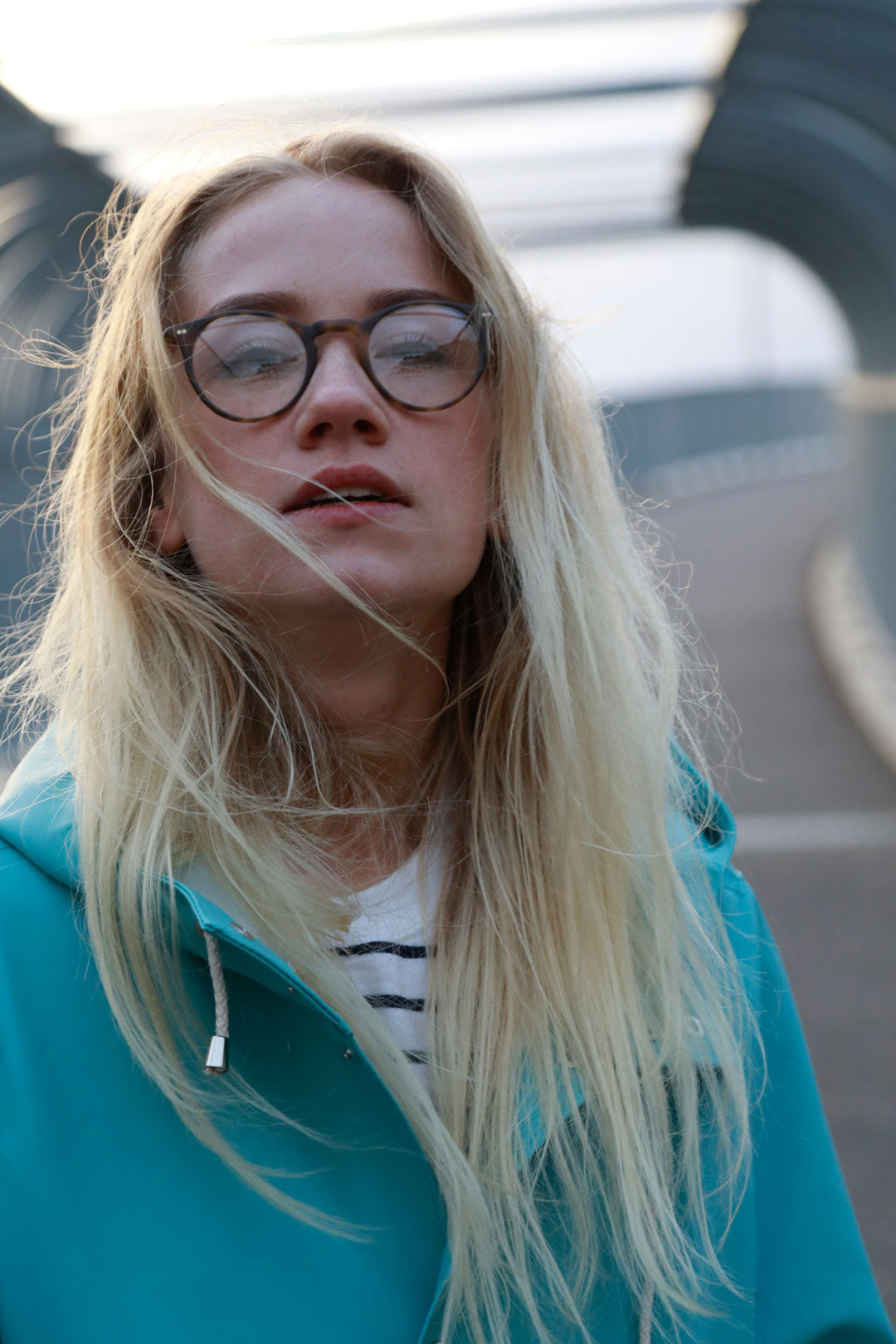 Blonde girl in pale blue jacket looking through round glasses