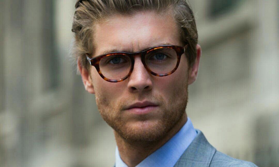 Blonde haired man wearing round tortoise acetate spectacles and grey suit
