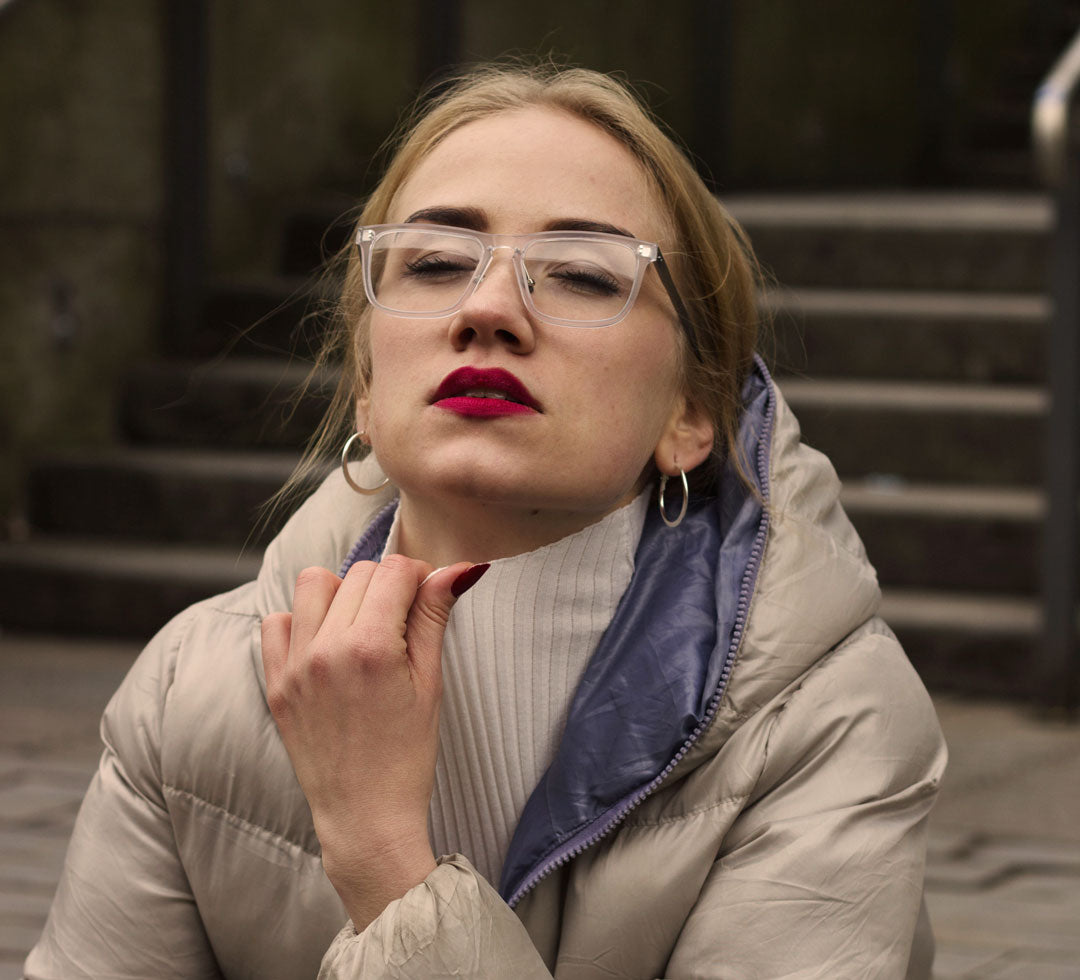 Blonde woman in street wearing puff jacket and frosted eyeglasses with her eyes closed and head back
