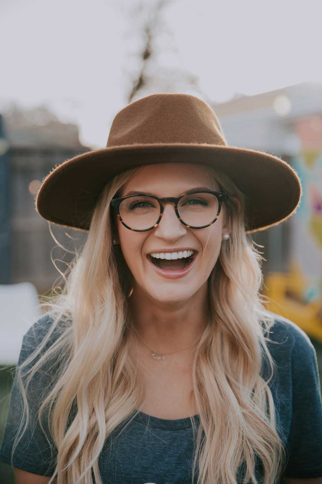 Blonde woman laughing wearing a hat and walnut shaped eyeglasses