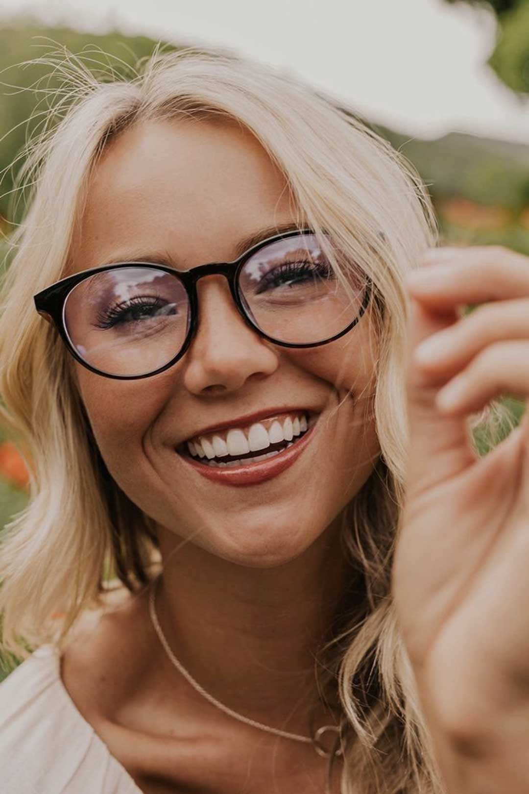 Blonde woman laughing wearing round black glasses frame