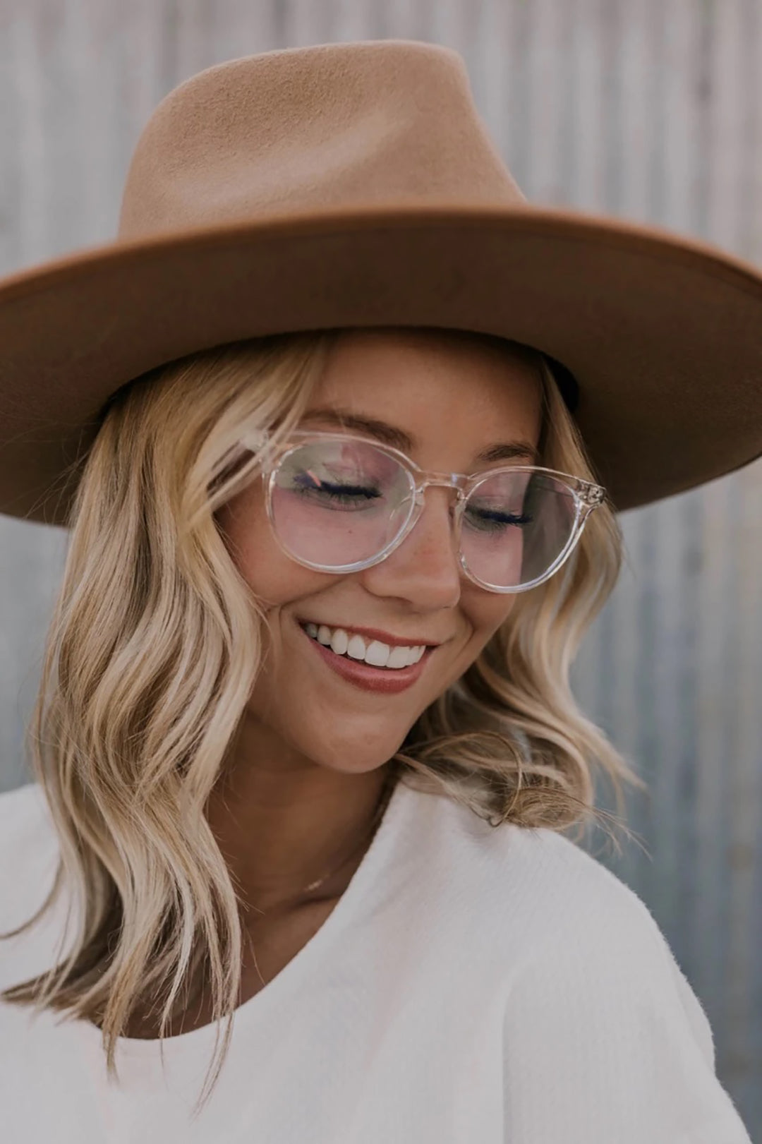 Blonde-woman-wearing-crystal-clear-eyeglasses-and-beige-hat-looking-downwards-smiling