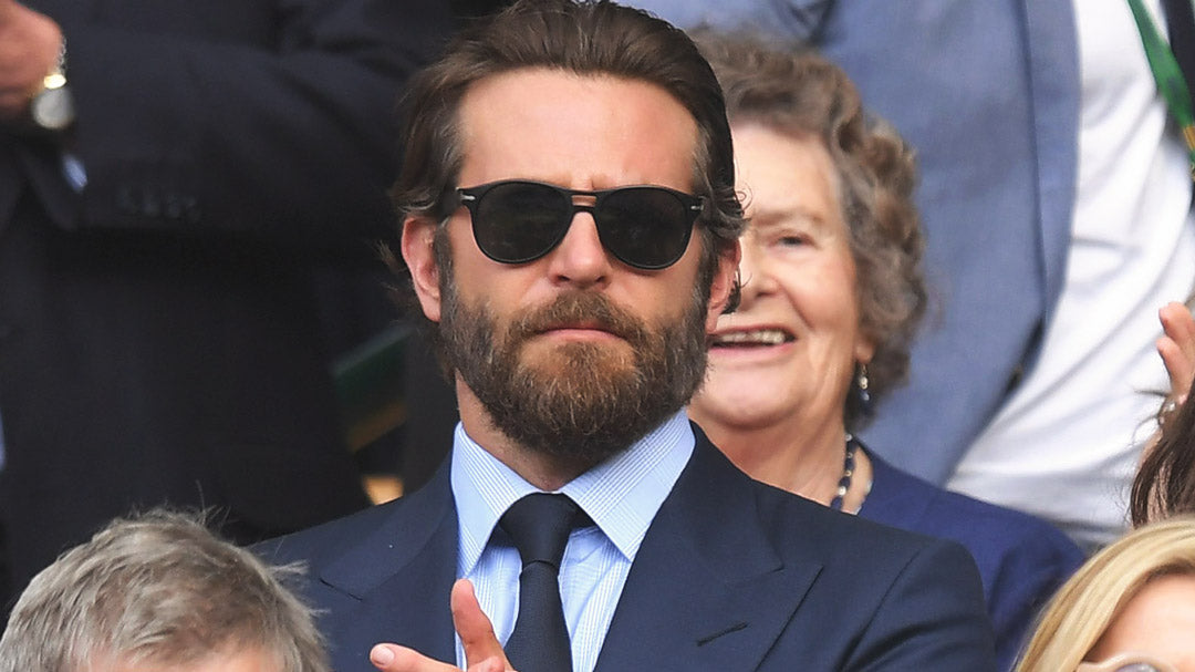 Bradley Cooper clapping at Wimbledon wearing blue suit and sunglasses