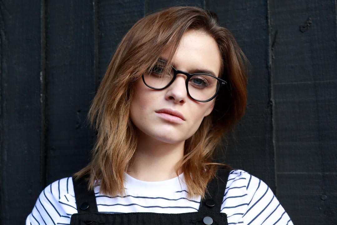 Brunette female against black wall wearing cat eye glasses