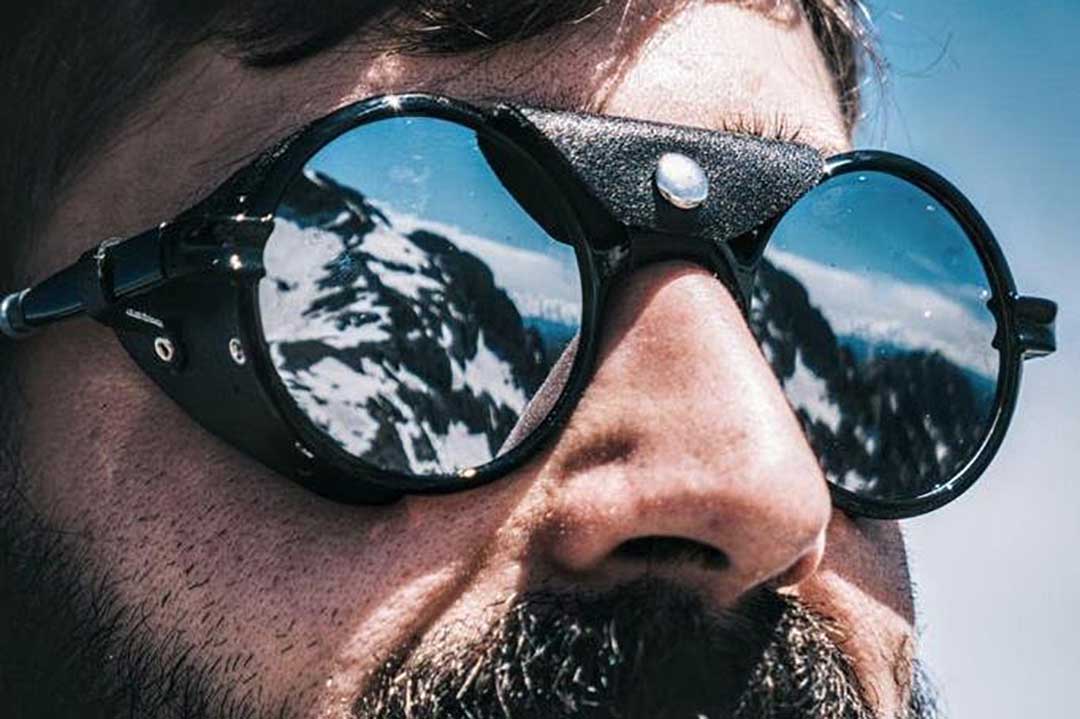 Close view of bearded man wearing round glacier sunglasses frame with mirrored lenses