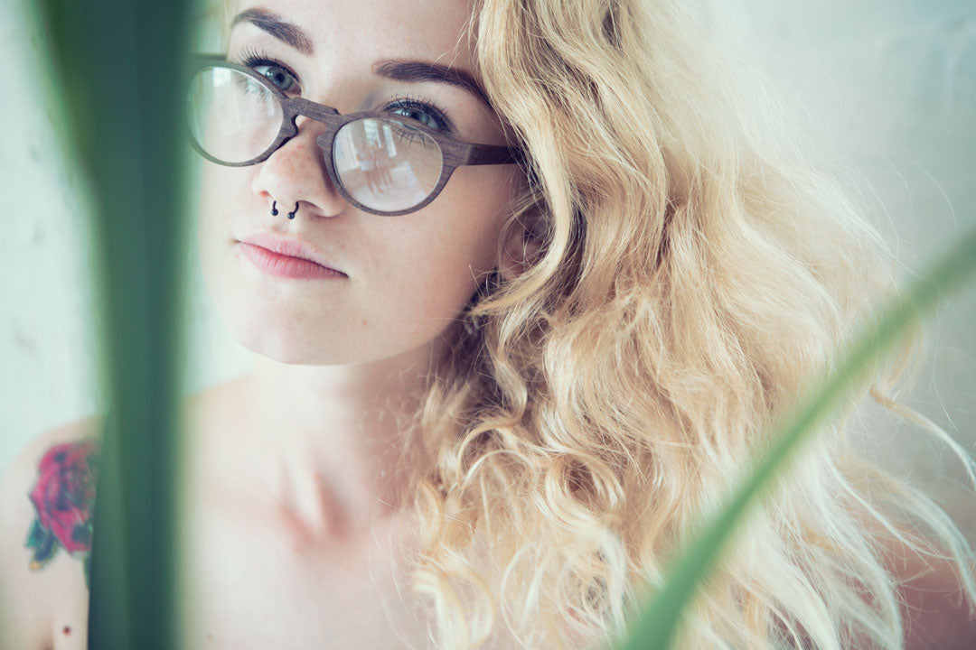 Close view of blonde female wearing round brown eyeglasses beside potted plant