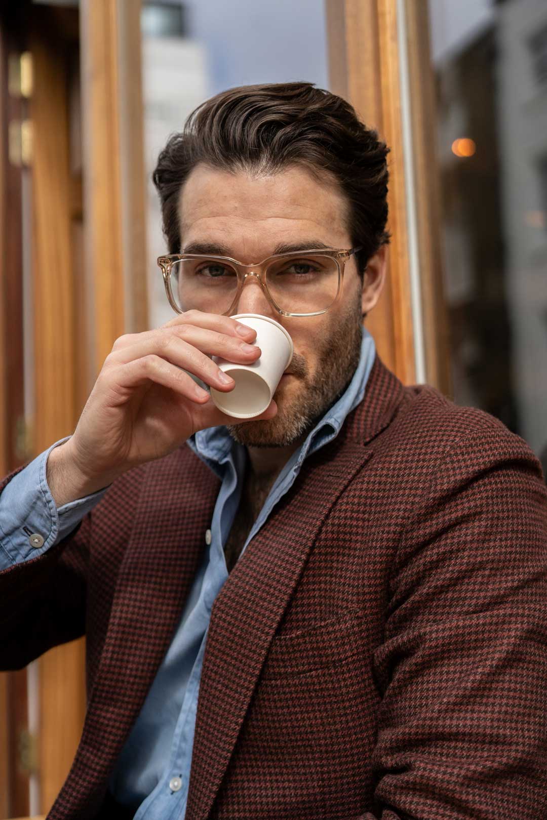 Close view of man wearing clear frame eyeglasses drinking coffee from white cup