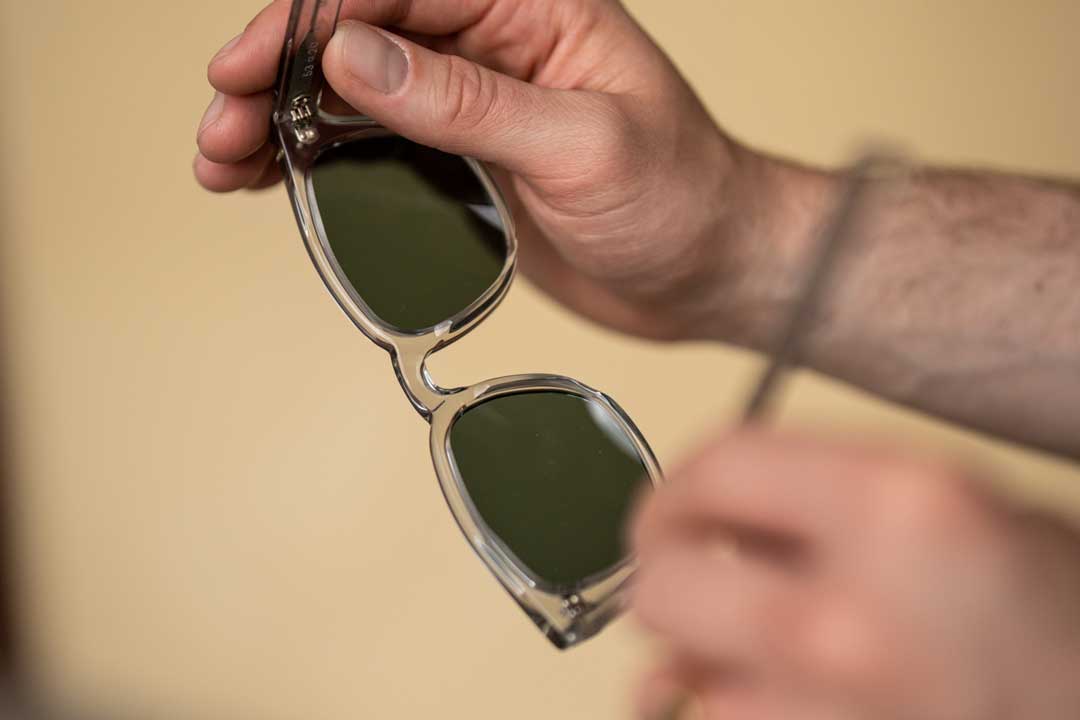 Close view of person holding clear frame sunglasses with green tinted lenses